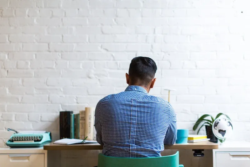 Someone working at a desk by a white brick wall